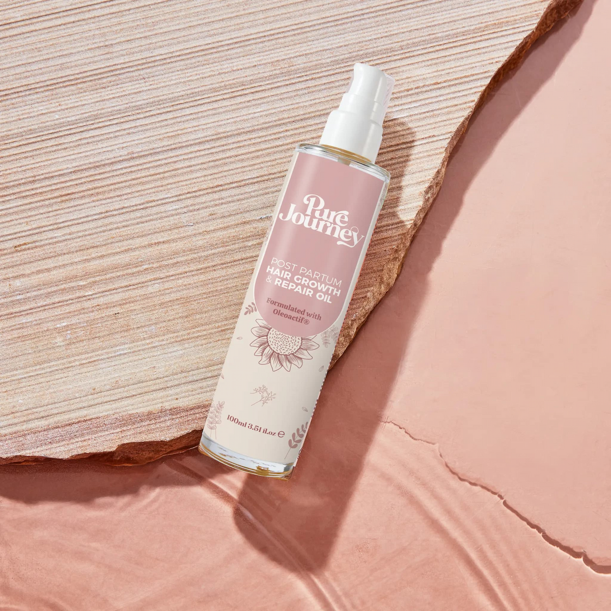 Pure Journey Post Partum Hair Growth and Repair Oil bottle on wooden surface with pink background